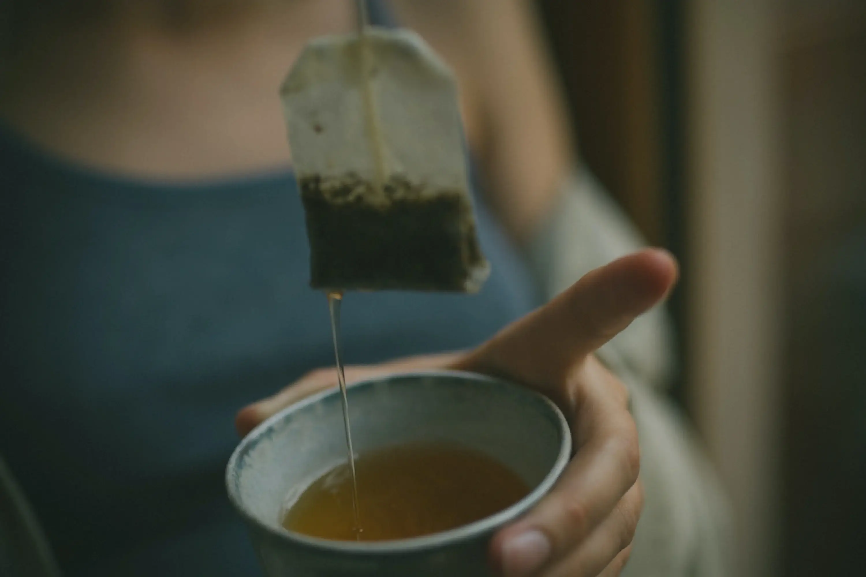 one hand holding a cup of tea and tea bag